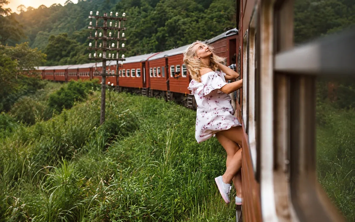 A passenger beside a red train travelling through lush green hill-country scenery