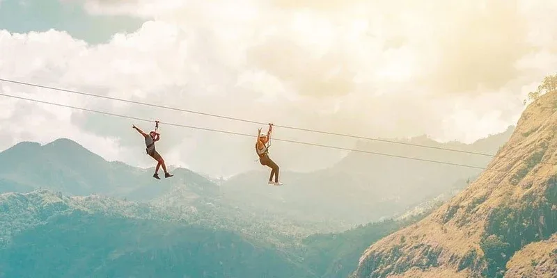 Two visitors ziplining above a mountain valley in Ella