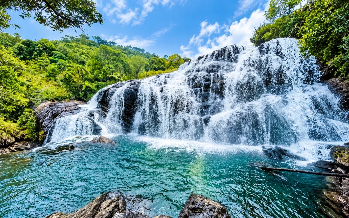 A broad waterfall cascading into a turquoise pool surrounded by lush green forest